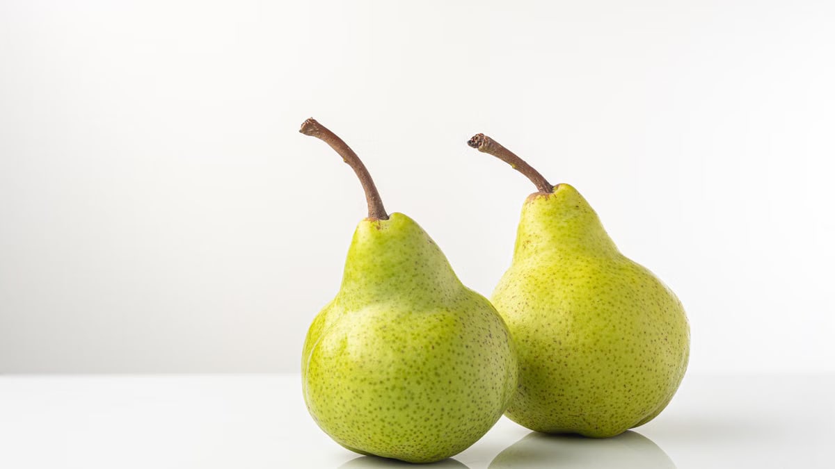 Close-up of two ripe green pears on a reflective white surface, symbolizing freshness and health.